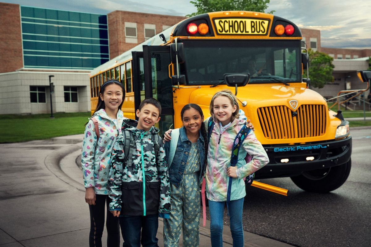 Four schoolkids posing in front of Navistar's electric school bus.