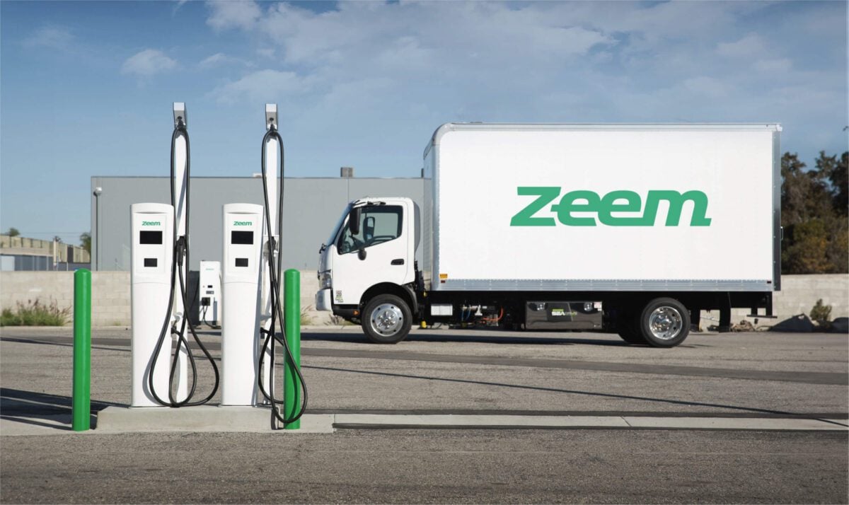 Zeem Solutions branded Class-8 truck, idled behind a Zeem Solutions branded charging station.